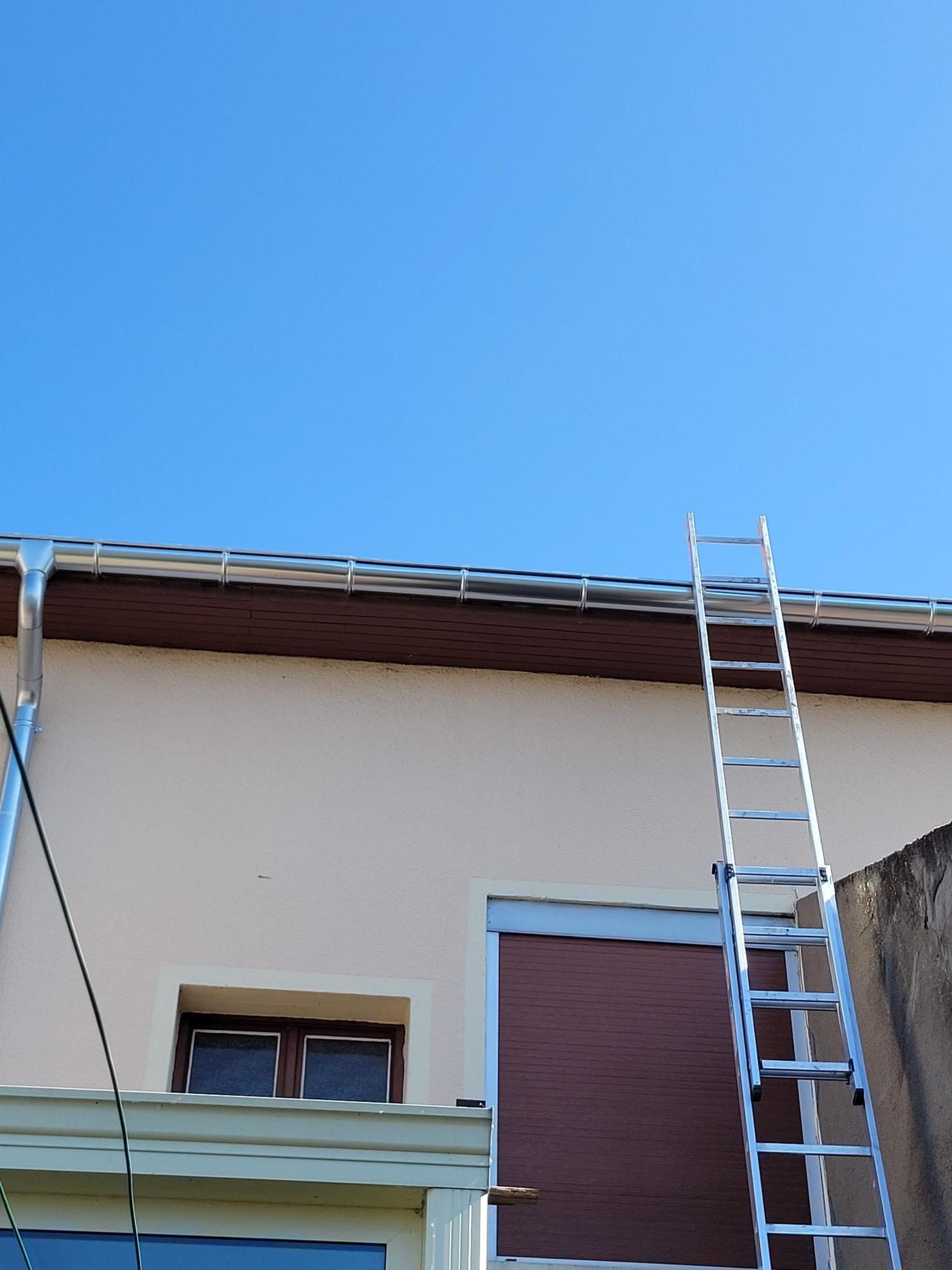 Gouttière neuve et échelle de couvreur contre une façade, sous un ciel bleu